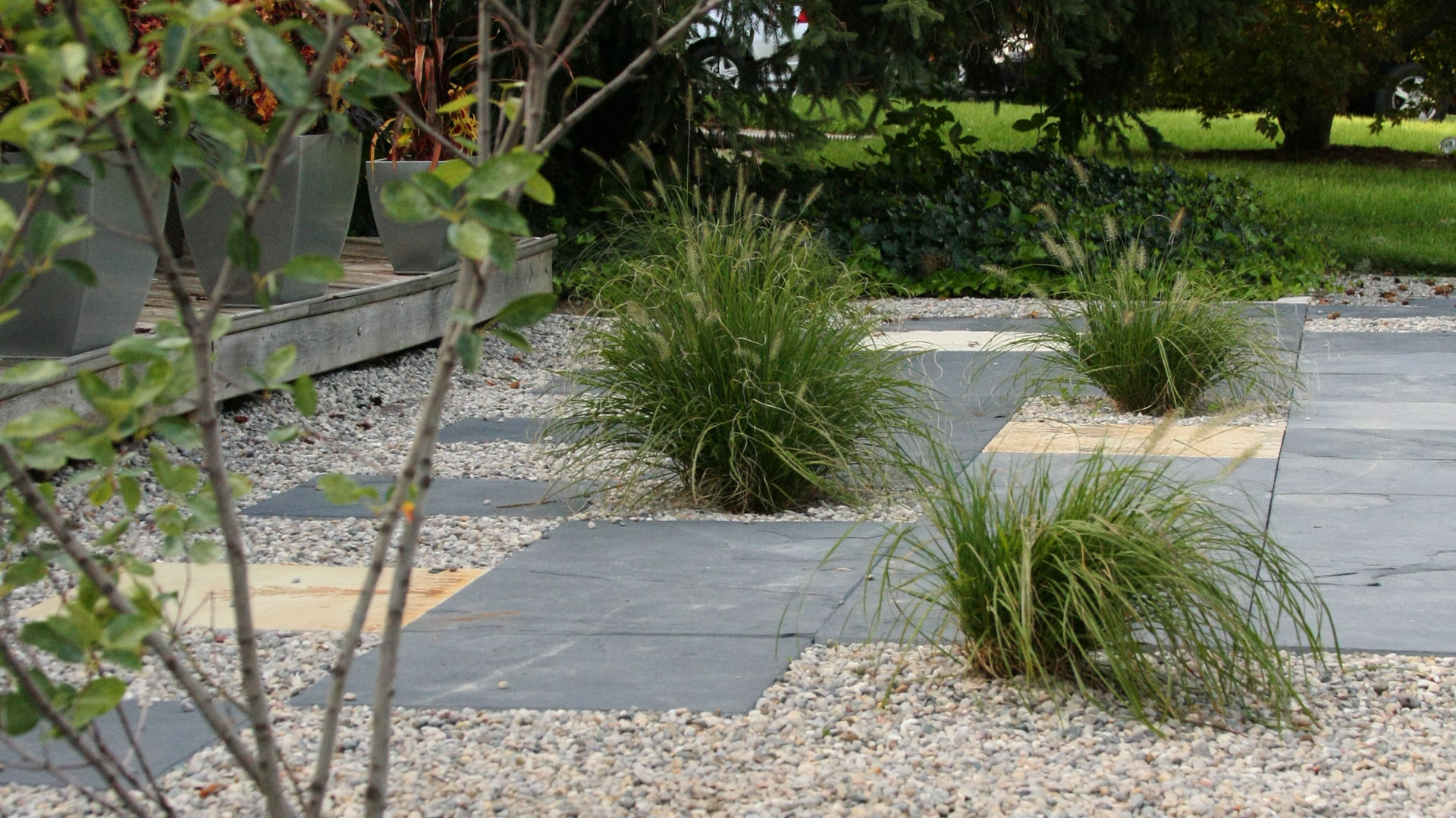 Stone slab tiles, pebbles, decorative tall grass. A small tree. Front yard landscape. Modern landscaping / hardscaping project in London Ontario.